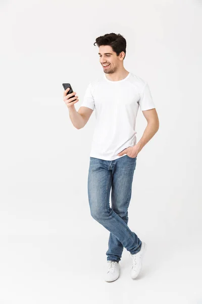 Emocionado joven feliz posando aislado sobre fondo blanco de la pared usando el teléfono móvil . — Foto de Stock