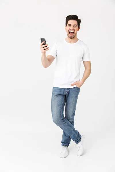 Excited happy young man posing isolated over white wall background using mobile phone. — Stock Photo, Image