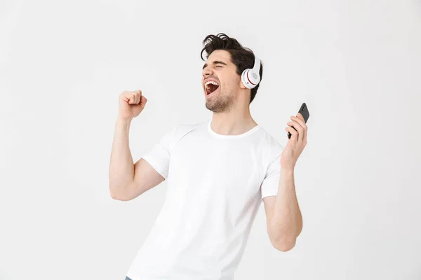 Emotioneel opgewonden jonge man poseren geïsoleerd over witte muur achtergrond luisteren muziek met koptelefoon. — Stockfoto