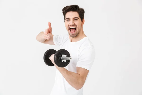 Emotional happy excited young man posing isolated over white wall holding dumbbell make exercise pointing. — Stock Photo, Image