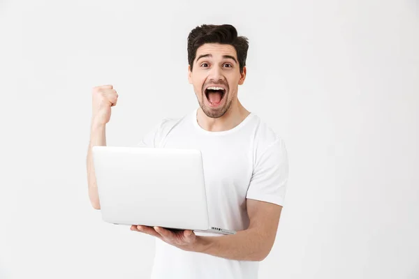 Feliz joven emocionado posando aislado sobre la pared blanca usando ordenador portátil hacer gesto ganador . — Foto de Stock