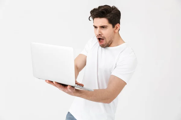 Scioccato confuso giovane uomo posa isolato su parete bianca utilizzando computer portatile . — Foto Stock