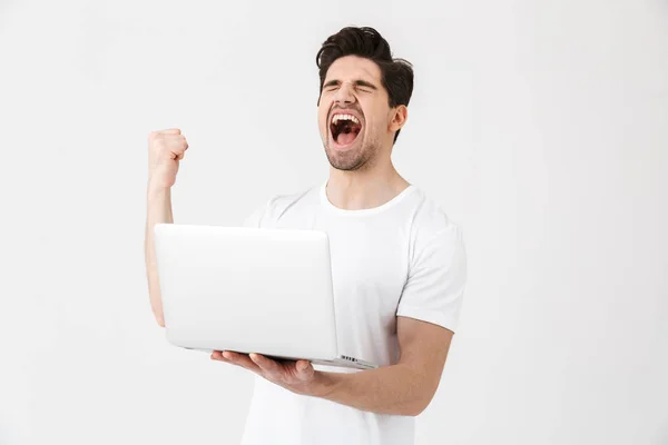 Boldog izgatott fiatalember pózol elszigetelt fehér fal segítségével laptop számítógépet, hogy győztes gesztus. — Stock Fotó