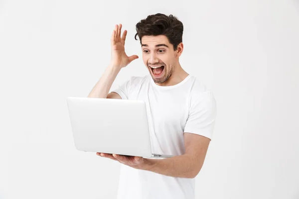 Impresionado joven emocionado posando aislado sobre la pared blanca usando ordenador portátil . —  Fotos de Stock