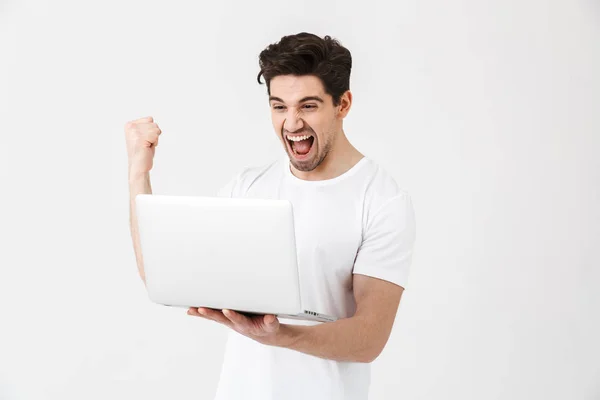 Щасливий збуджений молодий чоловік позує ізольовано над білою стіною за допомогою ноутбука робить жест переможця . — стокове фото