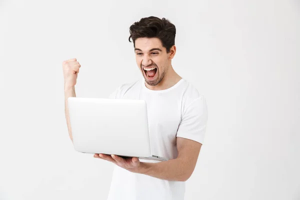 Feliz jovem animado posando isolado sobre a parede branca usando computador portátil fazer gesto vencedor . — Fotografia de Stock