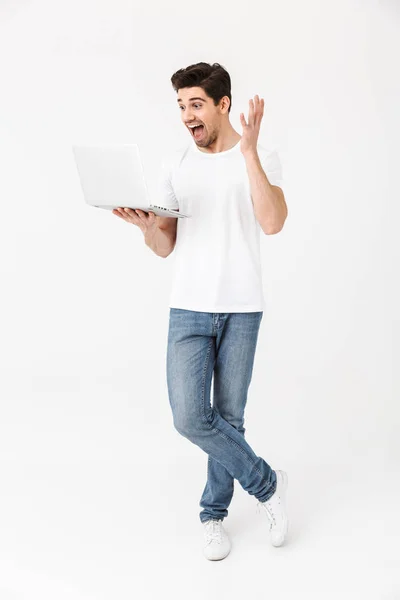 Schockierter aufgeregter junger Mann posiert isoliert mit Laptop über weißer Wand. — Stockfoto