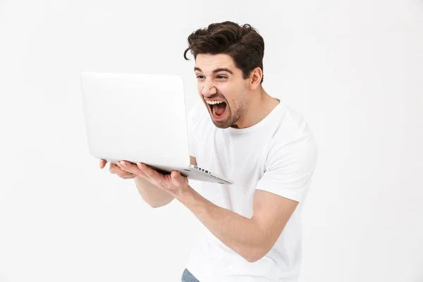 Кричащий молодой человек позирует изолированно над белой стеной с помощью ноутбука . — стоковое фото