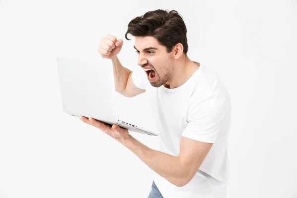 Кричущий молодий чоловік позує ізольовано над білою стіною за допомогою портативного комп'ютера . — стокове фото