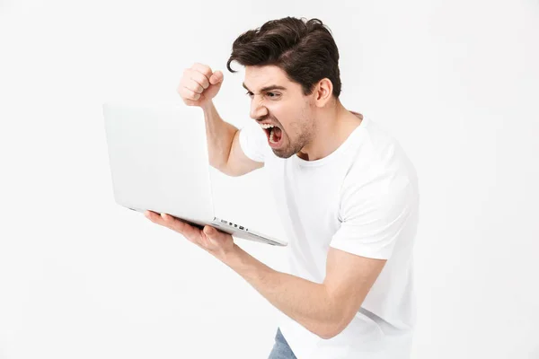 Gritando joven posando aislado sobre la pared blanca usando computadora portátil . —  Fotos de Stock