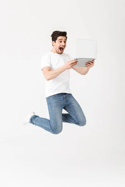 Счастливый возбужденный молодой человек позирует изолированные над белой стеной с помощью ноутбука компьютер прыжки . — стоковое фото