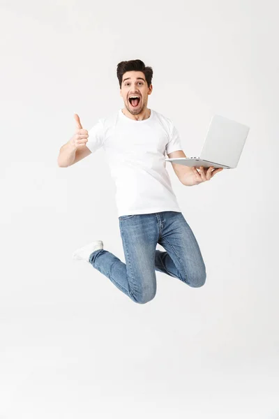 Glücklich aufgeregten jungen Mann posiert isoliert über weiße Wand mit Laptop Computer springen. — Stockfoto