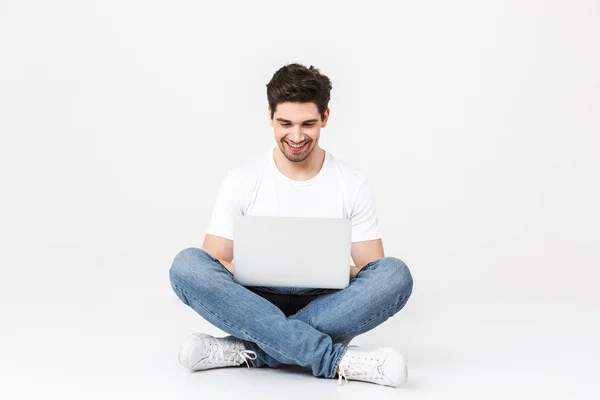 Podekscytowany młody człowiek pozowanie na białym ścianie za pomocą komputera przenośnego. — Zdjęcie stockowe
