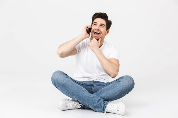 Feliz joven emocionado posando aislado sobre fondo de pared blanca hablando por teléfono móvil . — Foto de Stock