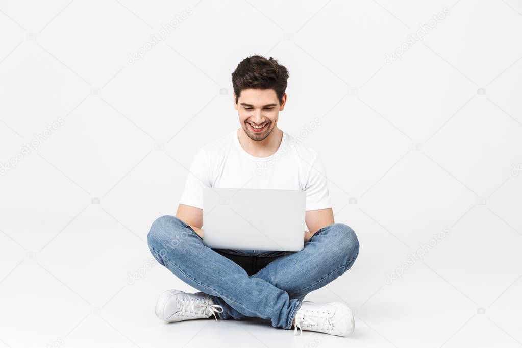 Excited young man posing isolated over white wall using laptop computer.