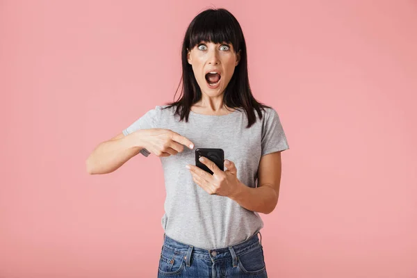 Verbazingwekkend opgewonden geschokt vrouw poseren geïsoleerd over licht roze achtergrond muur met behulp van mobiele telefoon. — Stockfoto