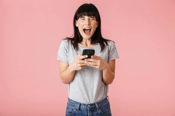 Increíble emocionada mujer sorprendida posando aislada sobre la pared de fondo rosa claro usando el teléfono móvil . — Foto de Stock