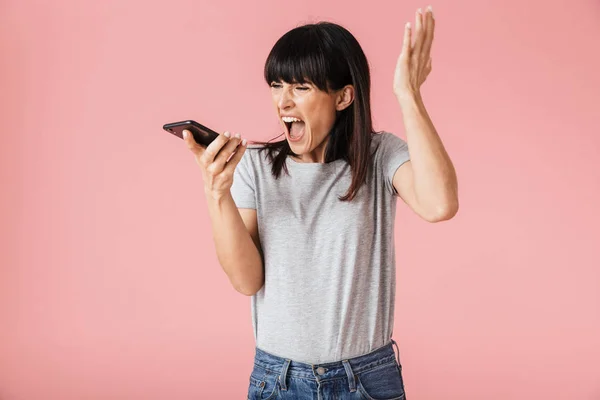 Hermosa mujer gritando disgustado posando aislado sobre la pared de fondo rosa claro hablando por teléfono móvil . — Foto de Stock
