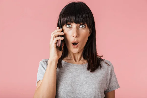 Emocionada mujer sorprendida posando aislada sobre la pared de fondo rosa claro hablando por teléfono móvil . — Foto de Stock