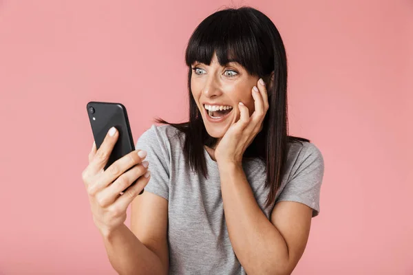 Amazing upphetsad lycklig kvinna poserar isolerade över ljusrosa bakgrund vägg med hjälp av mobiltelefon — Stockfoto