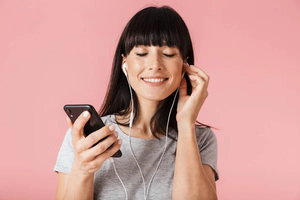 Eccitato felice donna posa isolato su parete di sfondo rosa chiaro utilizzando telefono cellulare musica di ascolto con auricolari . — Foto Stock