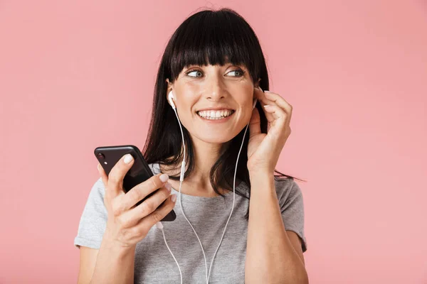 Eccitato felice donna posa isolato su parete di sfondo rosa chiaro utilizzando telefono cellulare musica di ascolto con auricolari . — Foto Stock