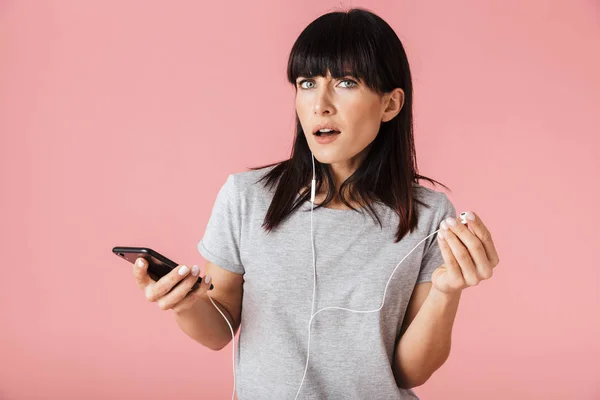 Žena, která se chová izolovaně přes růžovou zeď naslouchající hudbě s sluchovými telefony, se vás snaží vyslechnout. — Stock fotografie