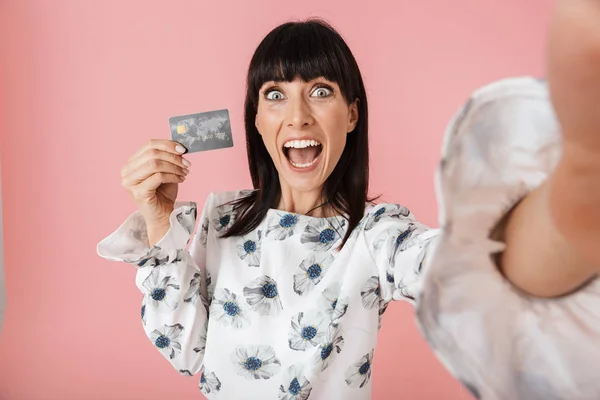 Frau posiert isoliert über rosa Wand Hintergrund Selfie von Kamera mit Kreditkarte. — Stockfoto