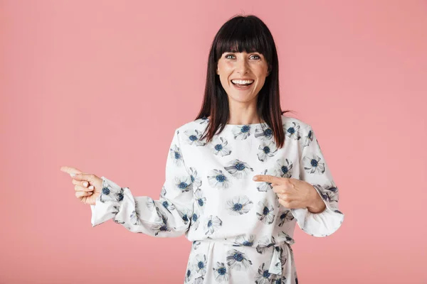 Opgewonden jonge vrouw poseren geïsoleerd over roze muur achtergrond wijzend. — Stockfoto