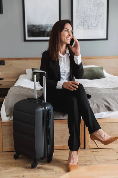 Молода ділова жінка в офіційному одязі вдома з валізою, що розмовляє мобільним телефоном . — стокове фото
