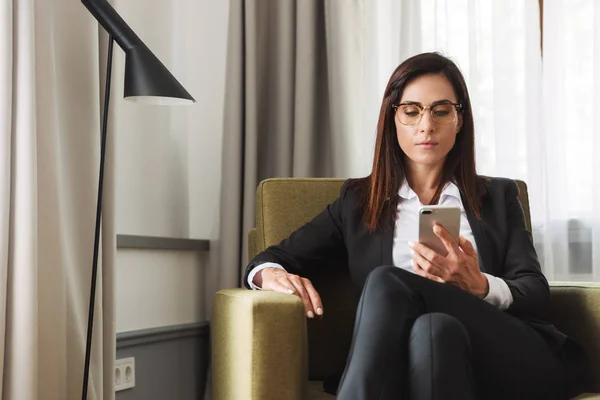 Hermosa mujer de negocios seria joven en ropa de desgaste formal en el interior de casa utilizando el teléfono móvil . —  Fotos de Stock