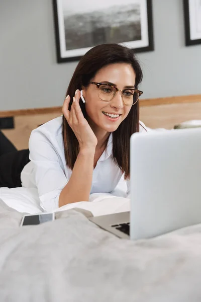 Retrato de encantadora mulher de negócios adulta usando laptop e fone de ouvido — Fotografia de Stock