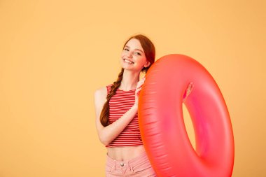 Gülümseyen genç güzel kızıl saçlı kadın kauçuk yüzük tutan sarı arka plan üzerinde izole poz.