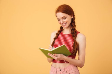 Mutlu genç güzel kızıl saçlı kadın kitap okuma tutarak sarı arka plan üzerinde izole poz.