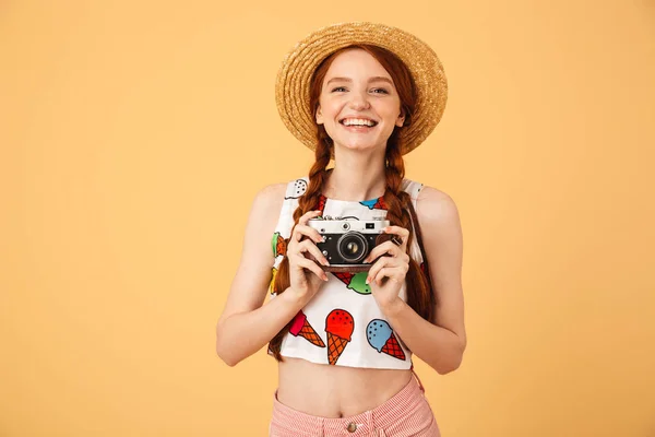 Щаслива молода красива руда жінка-фотограф турист одягнена в морозиво друкована футболка позує ізольовано на жовтому фоні тримає камеру . — стокове фото