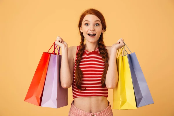 Shocked surprised young beautiful redhead woman posing isolated over yellow background holding shopping bags. — Stock Photo, Image