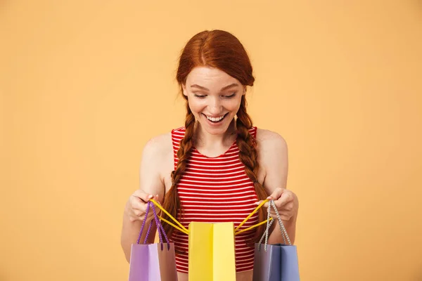 Megdöbbentette a fiatal, szép vöröshajú nő jelentő elszigetelt, mint a sárga háttér tartó bevásárló táskák. — Stock Fotó