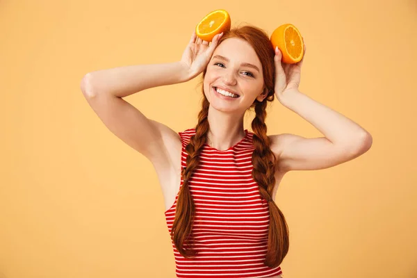 Joyeux jeune belle rousse femme posant isolé sur fond jaune tenant orange . — Photo