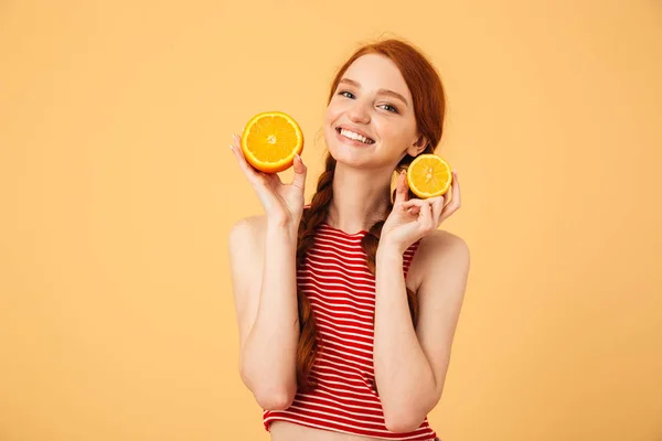 Feliz jovem mulher ruiva bonita posando isolado sobre fundo amarelo segurando laranja . — Fotografia de Stock