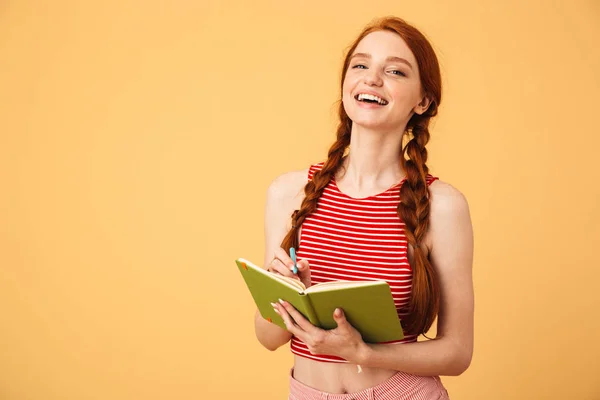 웃고 젊은 아름다운 빨간 머리 여자 포즈 고립 위에 노란색 배경 들고 책 읽기. — 스톡 사진