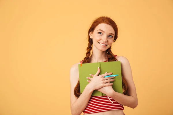 Dromen van jonge mooie roodharige vrouw poseren geïsoleerd over gele achtergrond houden boek lezen. — Stockfoto