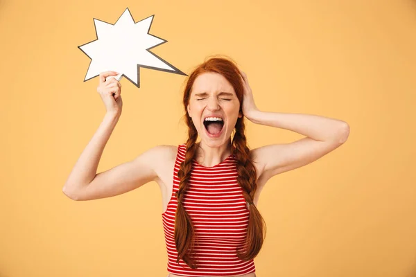 Gritando joven hermosa pelirroja posando aislada sobre fondo amarillo sosteniendo la burbuja del habla . — Foto de Stock