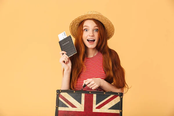 Opgewonden schattig jong mooi redhead vrouw poseren geïsoleerd over gele achtergrond houden koffer en paspoort met kaartjes — Stockfoto