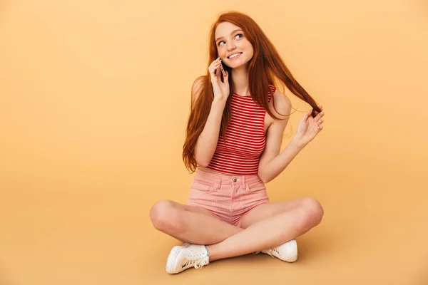 Jovem alegre bela ruiva posando isolado sobre fundo amarelo falando por telefone celular . — Fotografia de Stock