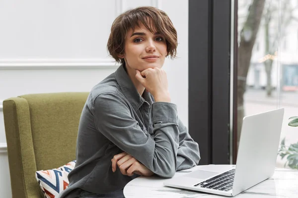 Glad ung student kvinne sitter på kafeen innendørs med laptop-datamaskin . – stockfoto