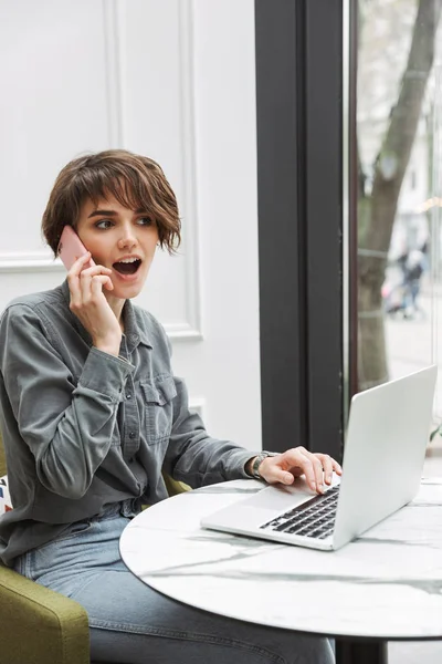 Shocked excited young pretty business student woman sitting in cafe indoors using laptop computer coworking.