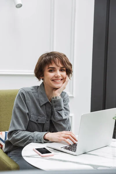 Feliz sorrindo jovem bonita estudante de negócios mulher sentada no café dentro de casa usando computador portátil coworking . — Fotografia de Stock