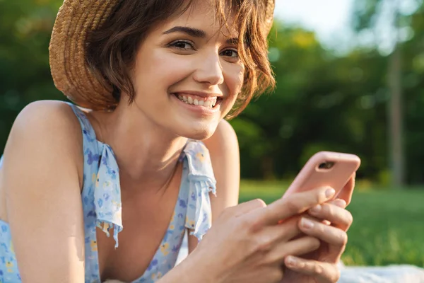 Mooie gelukkige jonge mooie vrouw in groen park buitenshuis met behulp van mobiele telefoon. — Stockfoto