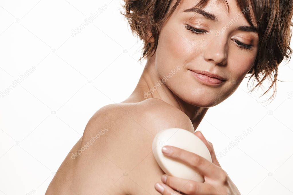 Pleased tender young pretty woman with healthy glowy skin posing isolated over white wall background holding soap take care of her skin washing body.