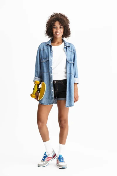 Mujer africana posando aislada sobre fondo blanco de pared con monopatín . — Foto de Stock